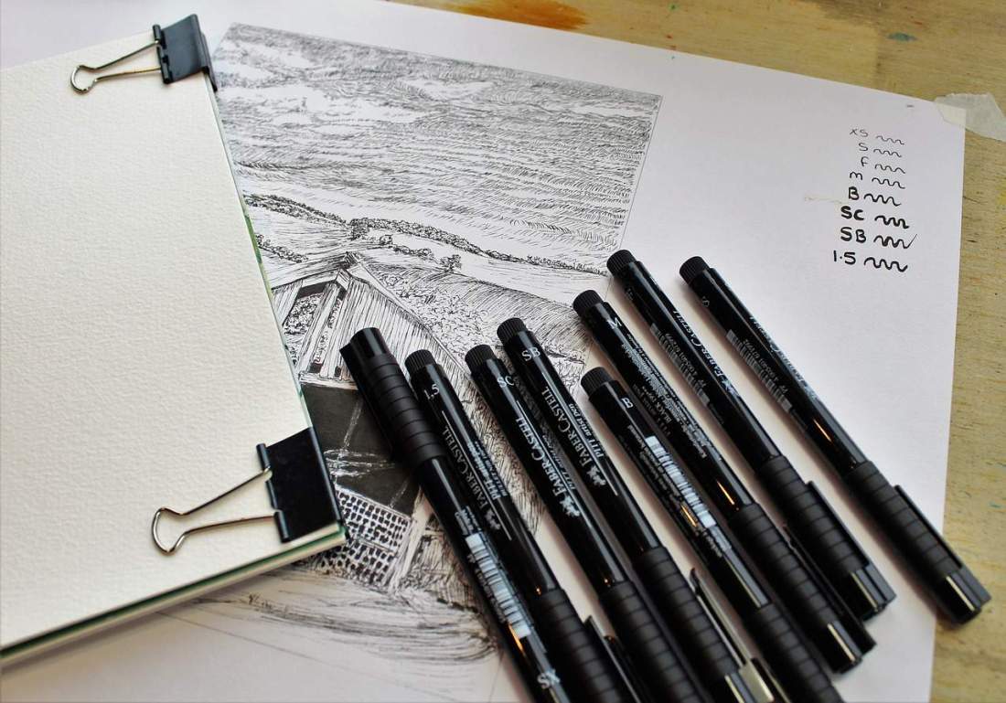 A photograph of a sketchbook and technical faber castell ink pen.